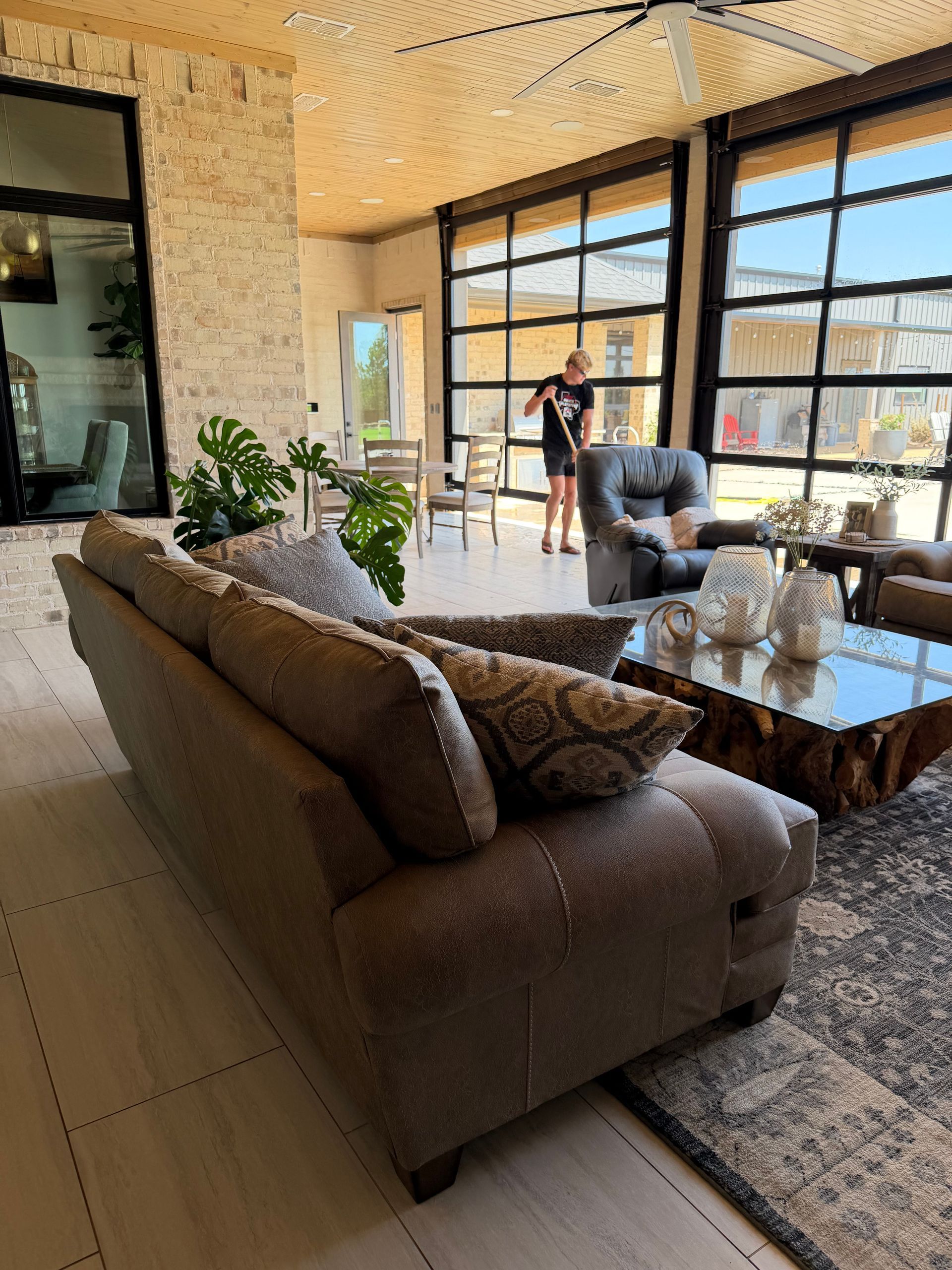 Modern living room with a brown sofa, glass coffee table, and large windows overlooking a balcony.