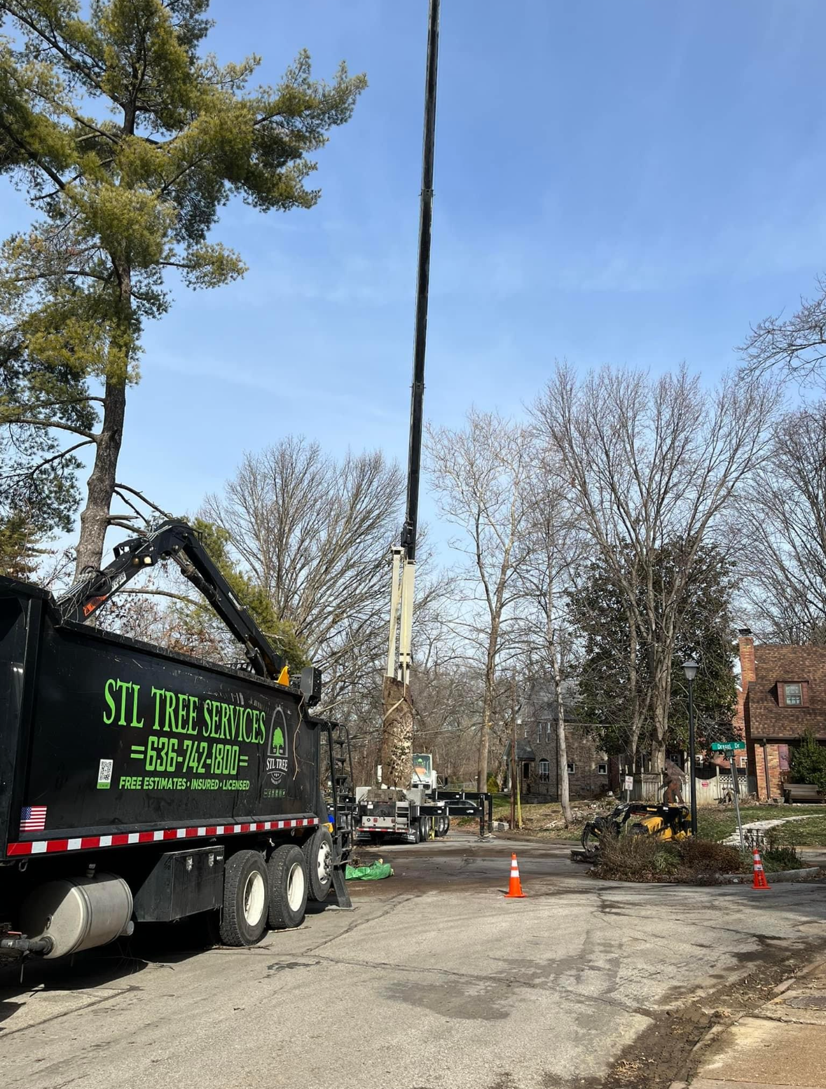 A tree being removed on a residential street by a truck with a boom lift.