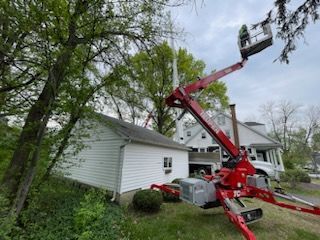 Red boom lift trimming a tree near a white garage and house on a cloudy day.