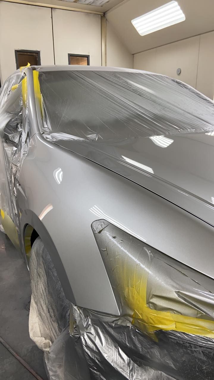 A silver car is being painted in a paint booth