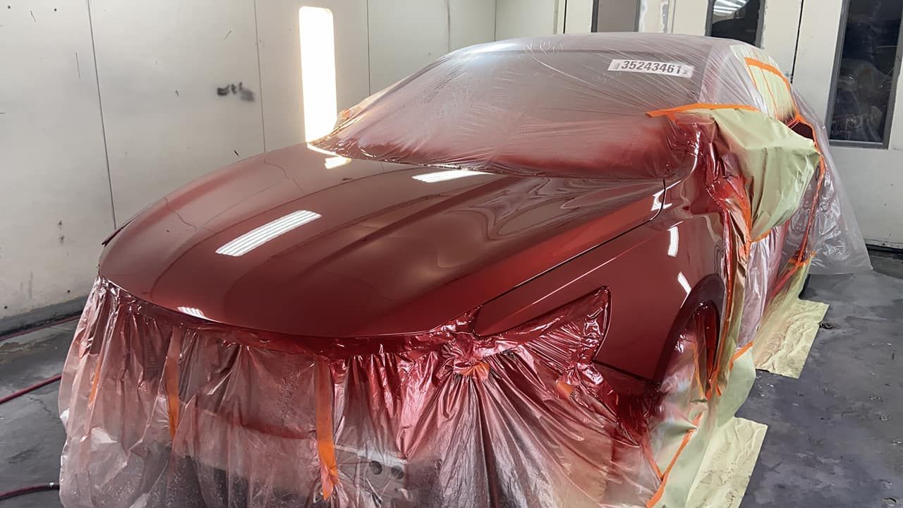 A red car is covered in plastic in a paint booth