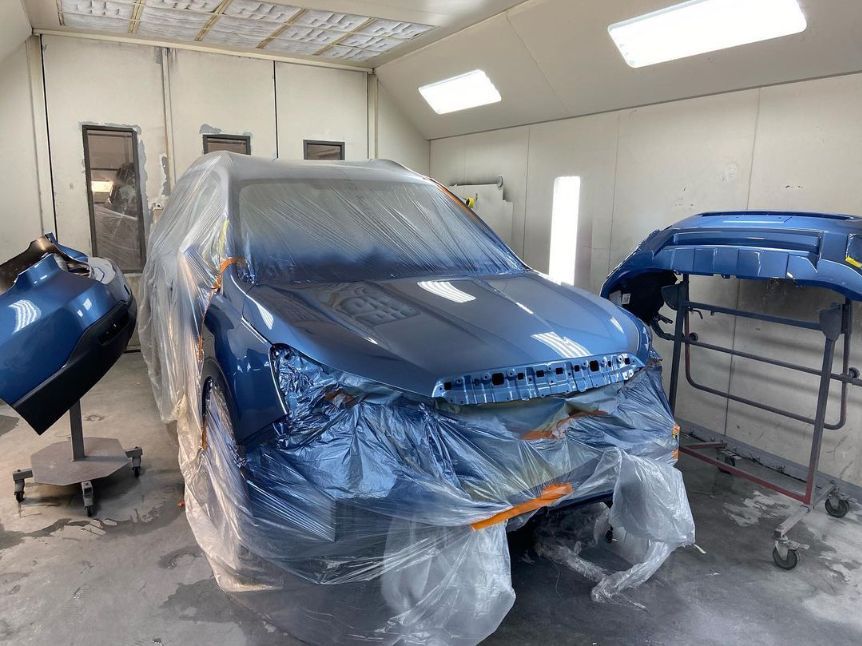 A blue car is being painted in a paint booth