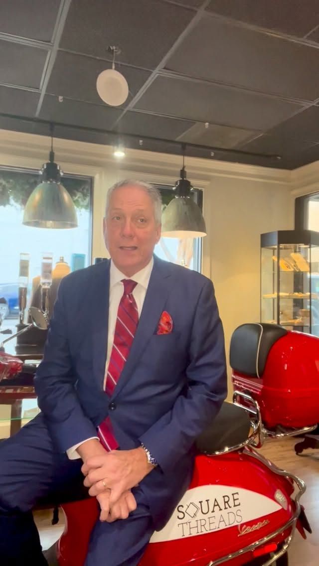 Man in suit sitting on red scooter, indoors, smiling.