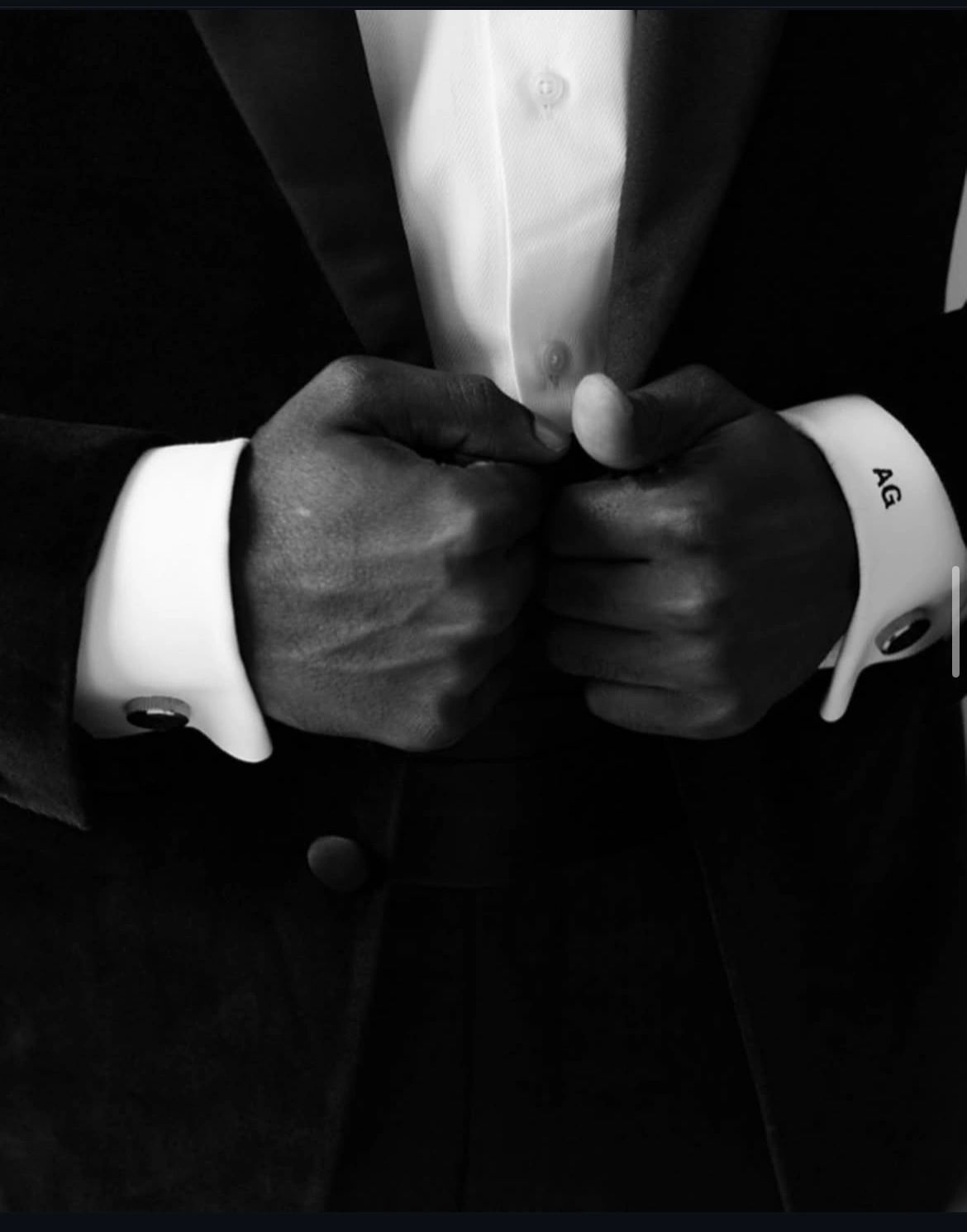 Close-up of a person's hands in a tuxedo. One cufflink displays the initials