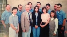 Group of nine people standing indoors, smiling for a formal portrait.