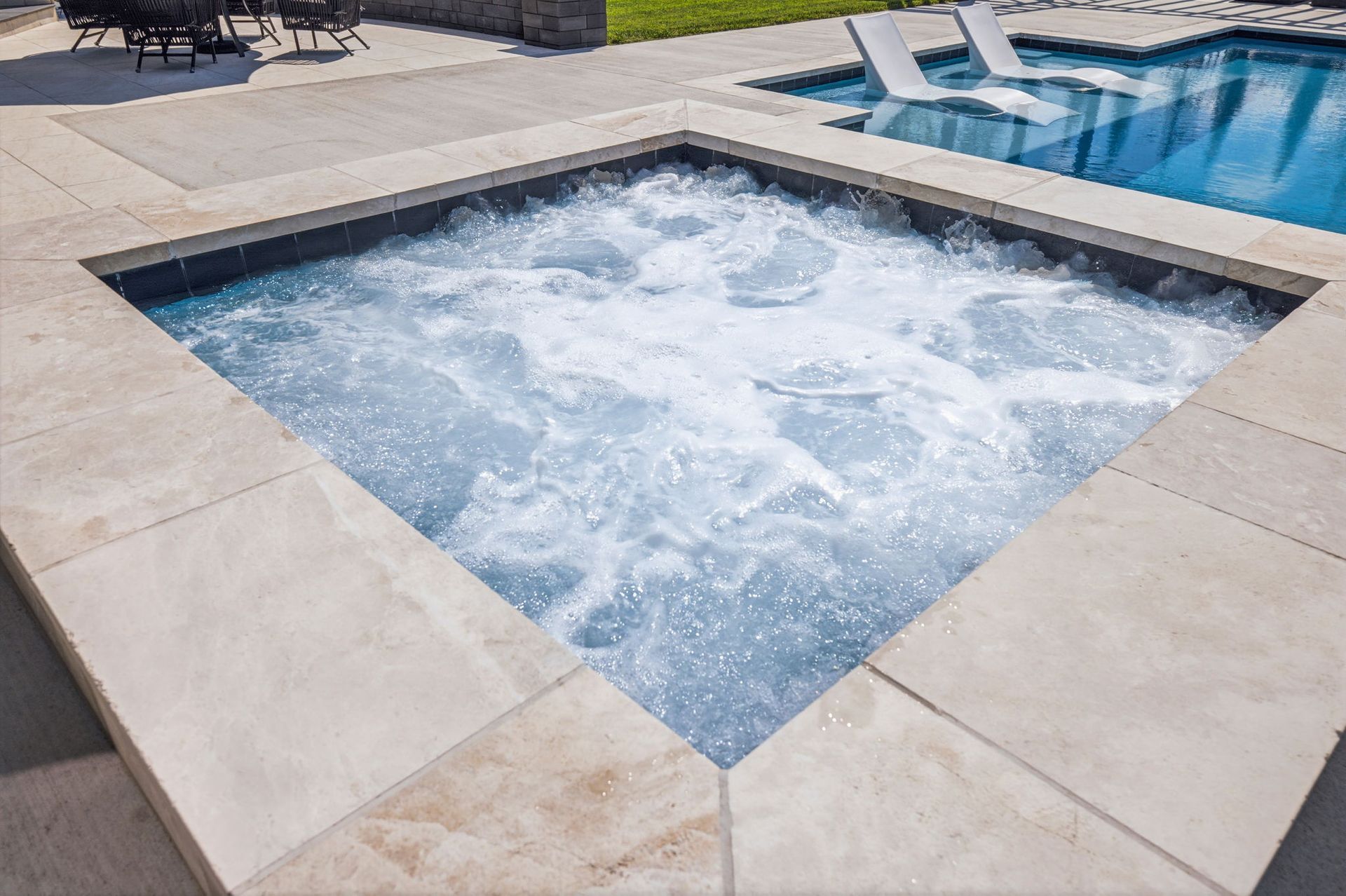 Square hot tub bubbling beside a blue swimming pool on a stone patio