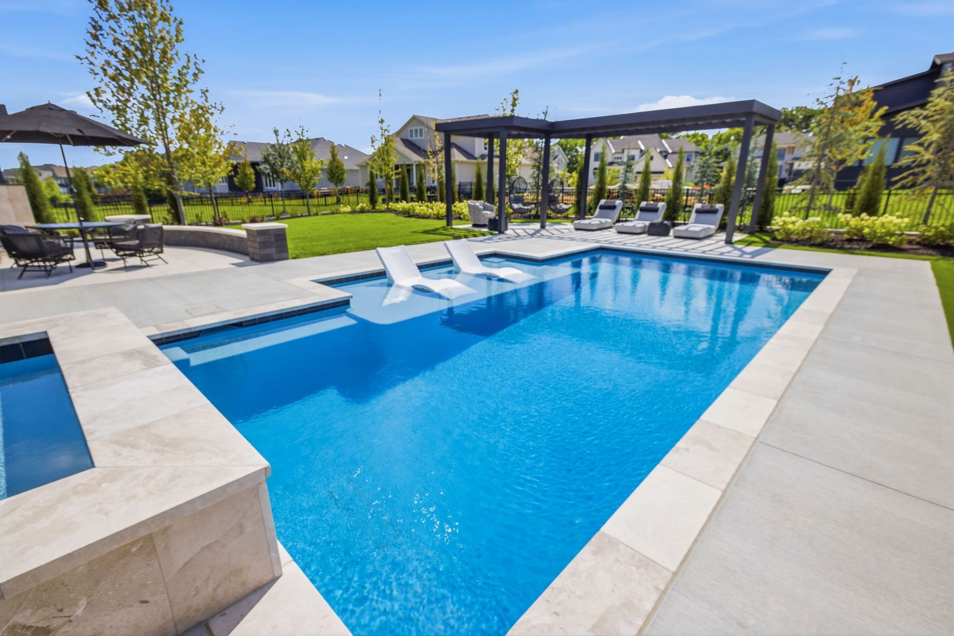 Modern backyard pool with blue water, lounge chairs, pergola, and landscaped patio