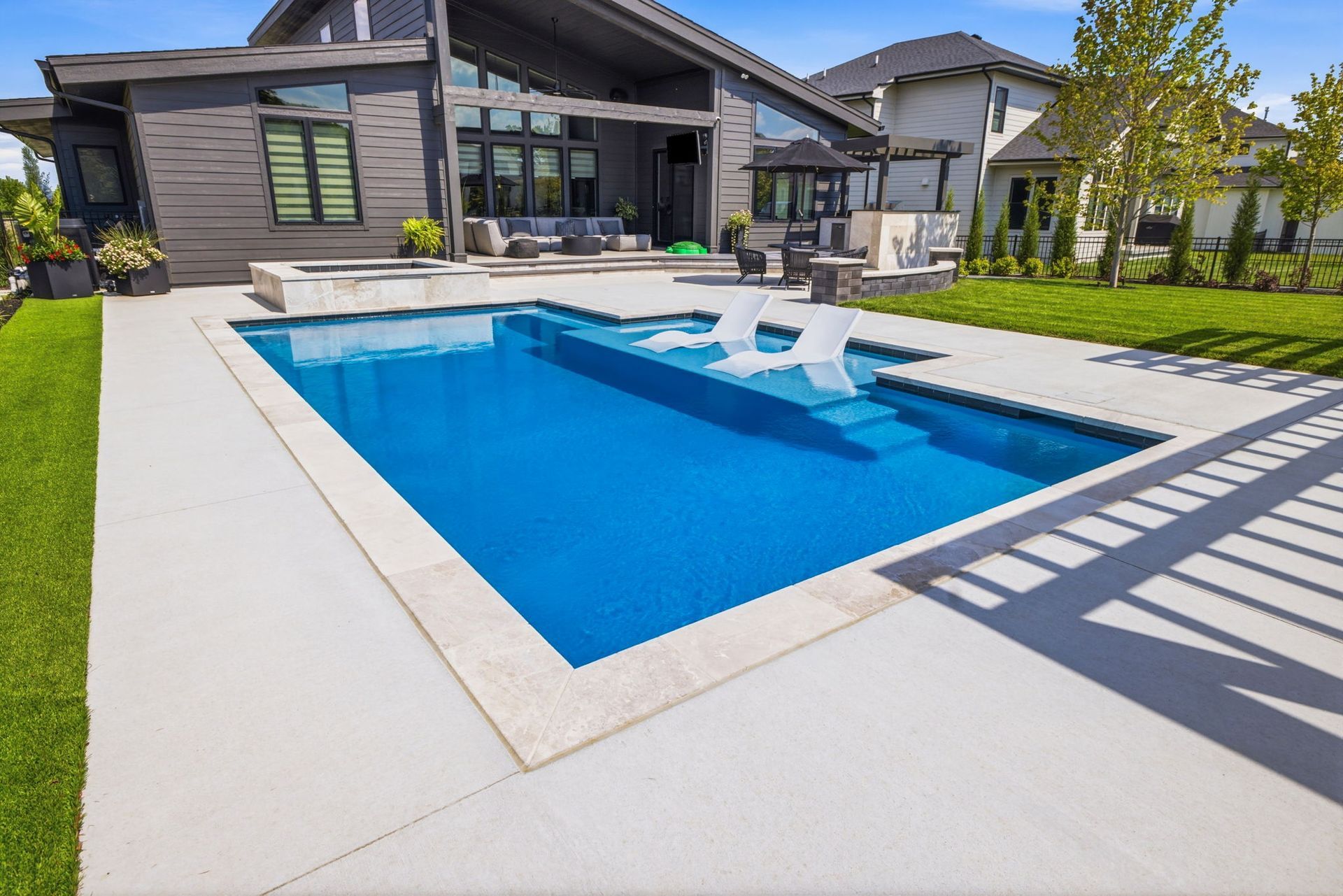 Modern backyard with a blue rectangular swimming pool beside a contemporary house and patio area