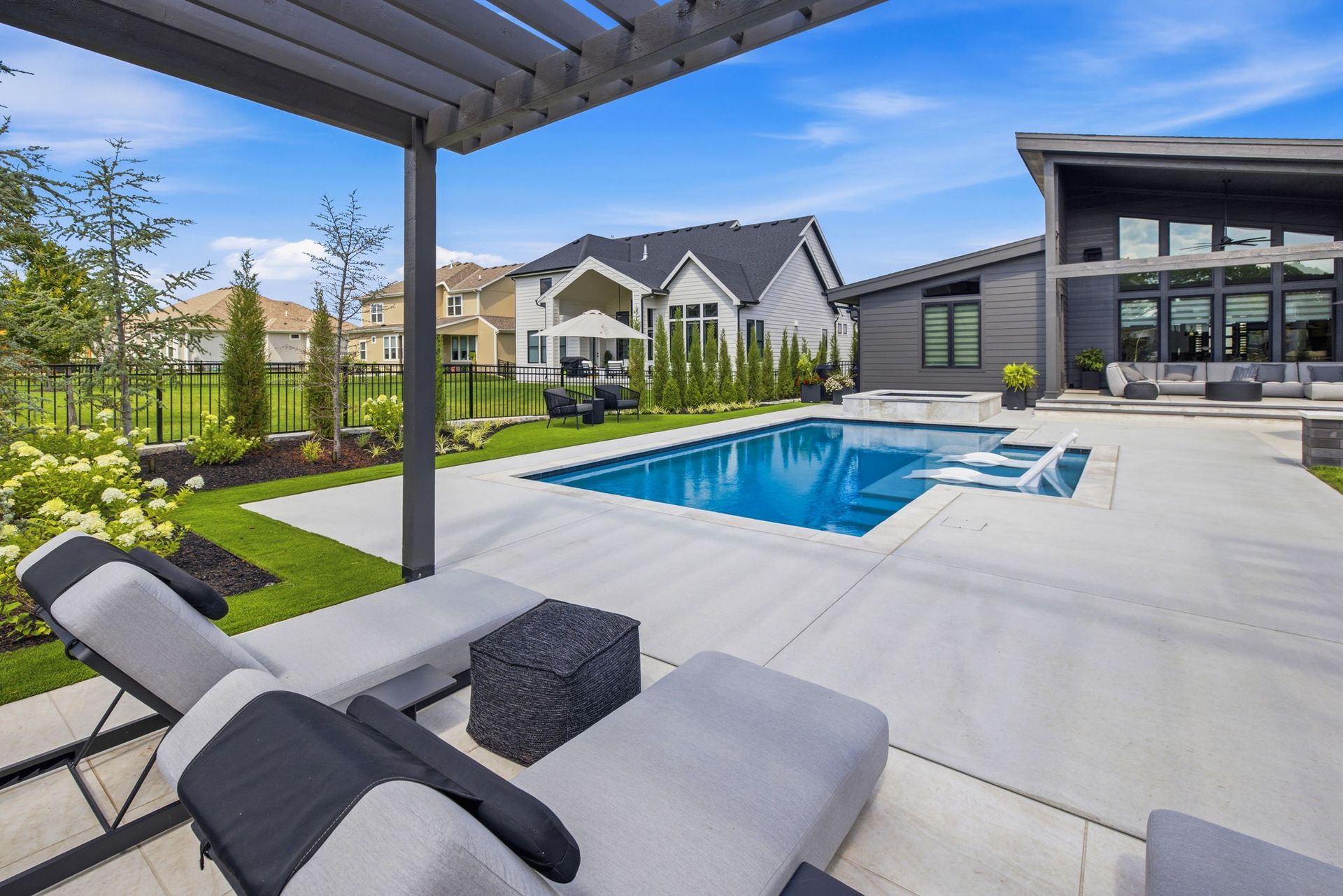 Modern backyard with a swimming pool, lounge chairs, pergola, and contemporary house.