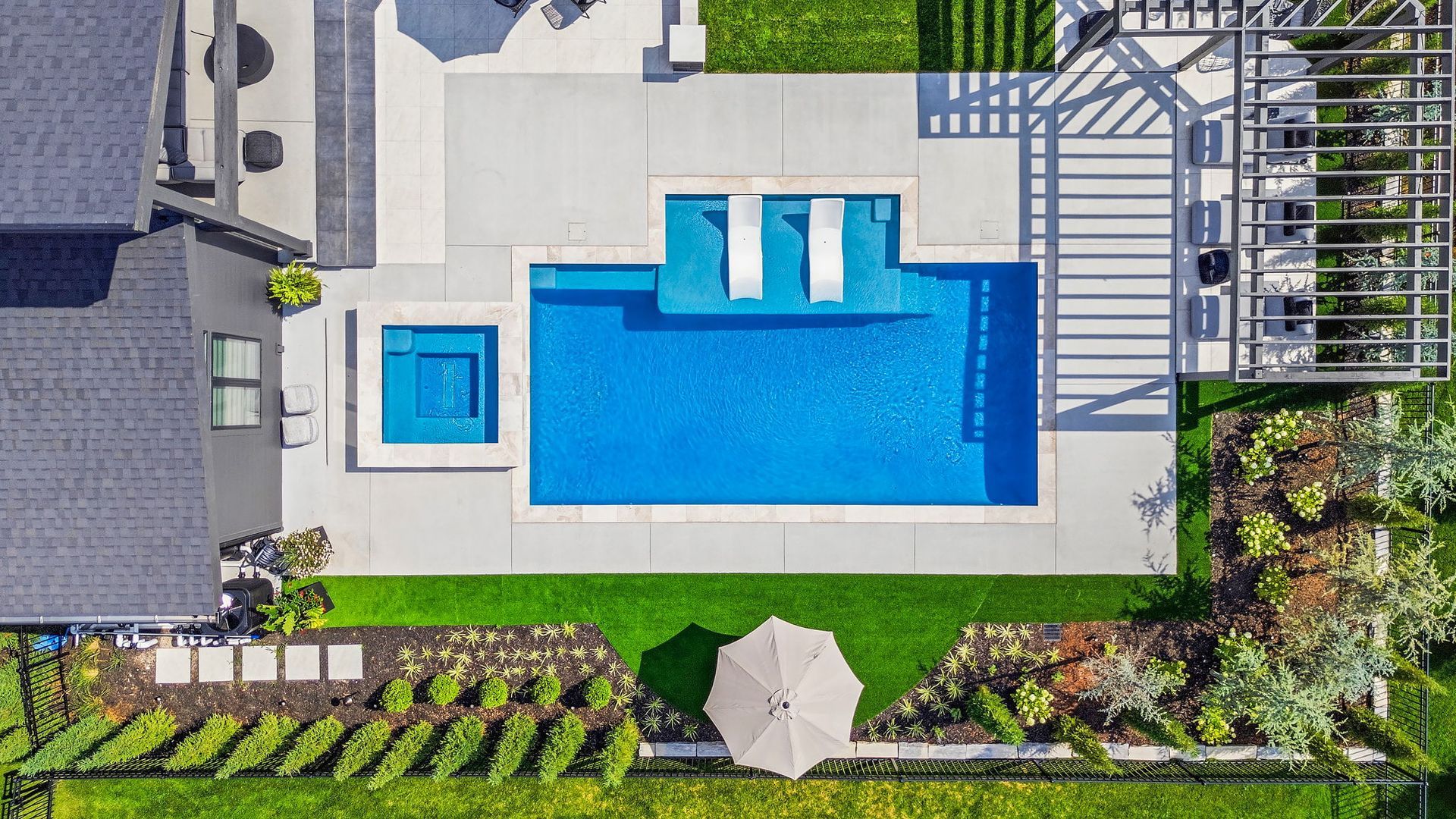 Overhead view of a backyard with a rectangular swimming pool, spa, patio, and lush landscaping.