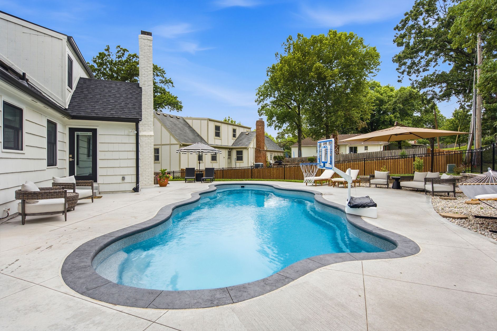 Outdoor patio with a small blue swimming pool, lounge chairs, and a shaded seating area beside apartment buildings