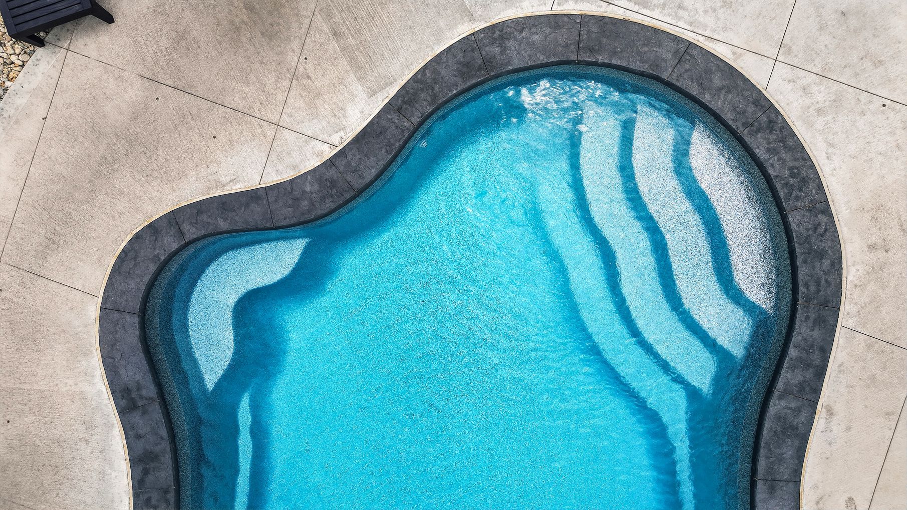 Top view of a blue swimming pool with dark border and light ripples at the edge