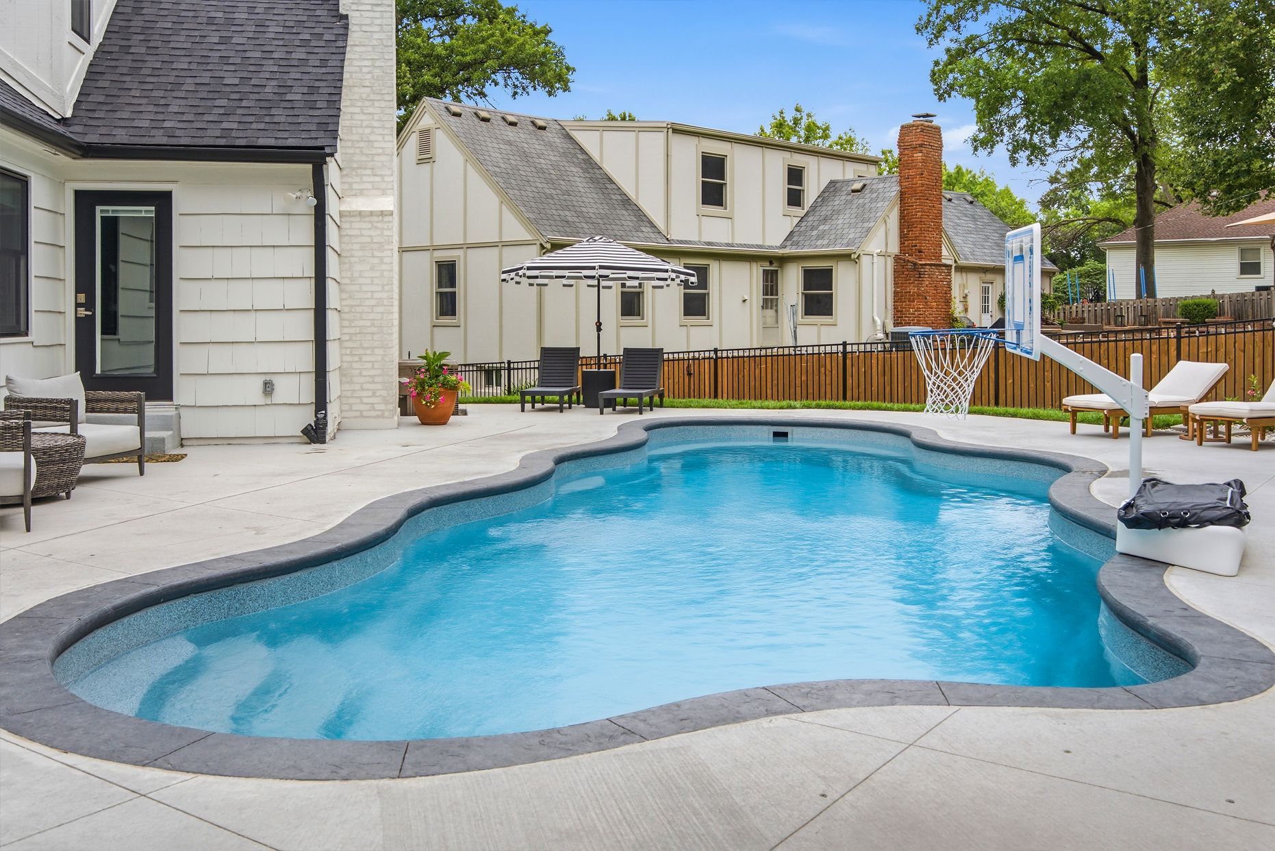Backyard pool with blue water beside a house and patio furniture under a cloudy sky