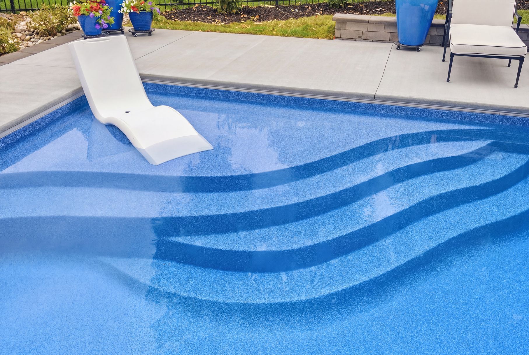 Blue swimming pool with a white slide and patio chairs nearby