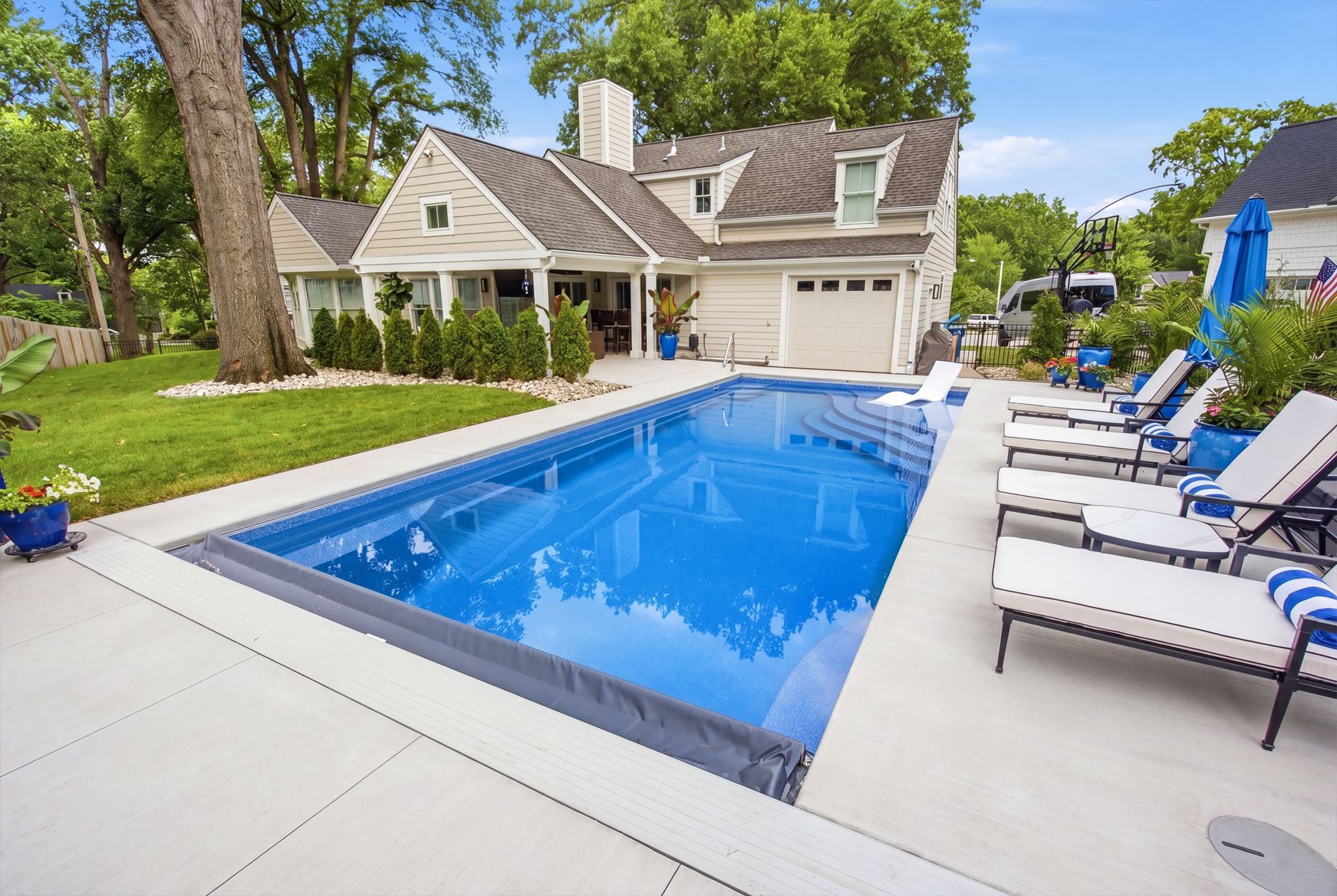Backyard with a blue swimming pool, lounge chairs, and a house surrounded by trees