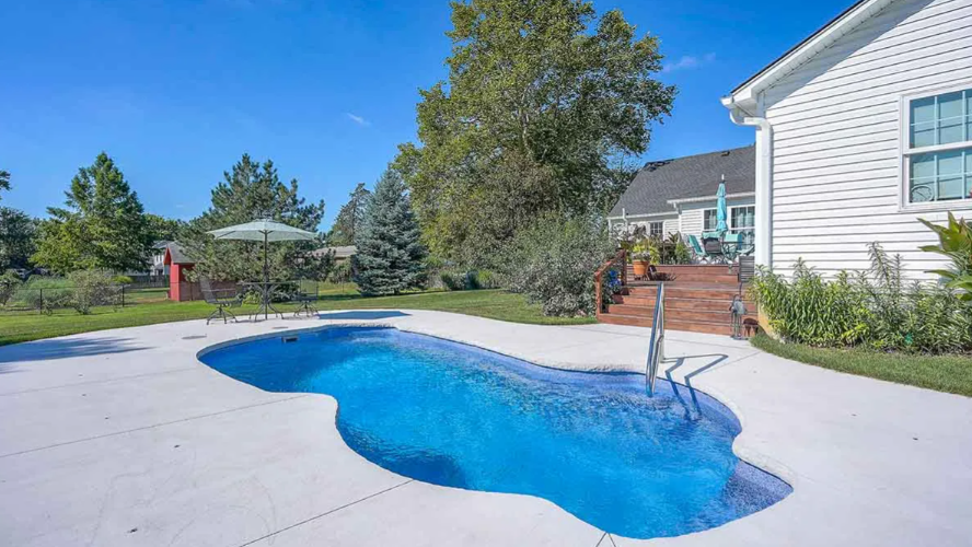 Backyard with a blue, freeform pool and a white house under a sunny sky.