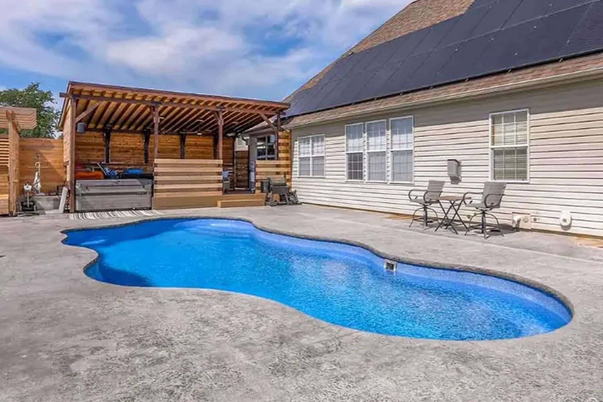 Backyard with a blue, freeform pool, patio, and covered deck next to a house with solar panels.