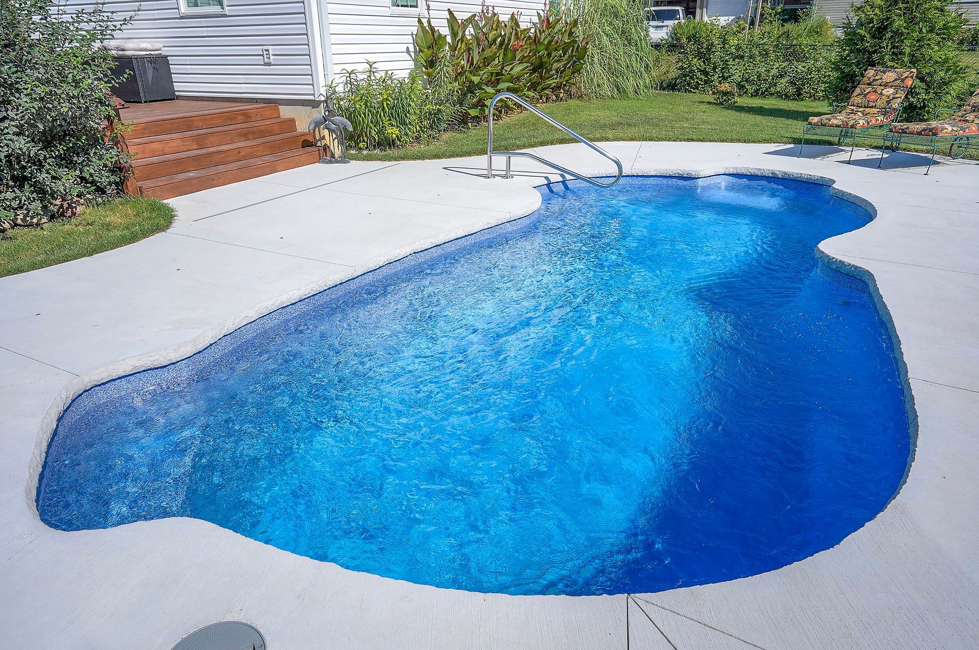 A blue-tiled, irregularly-shaped swimming pool surrounded by a concrete patio and grass.