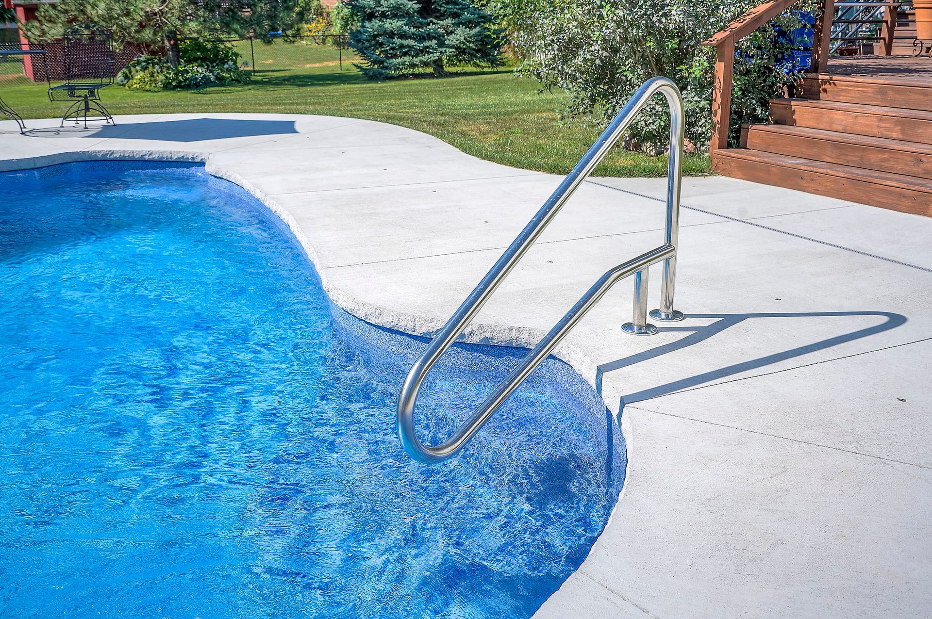 Swimming pool with a stainless steel handrail, white concrete edging, and a wooden deck.