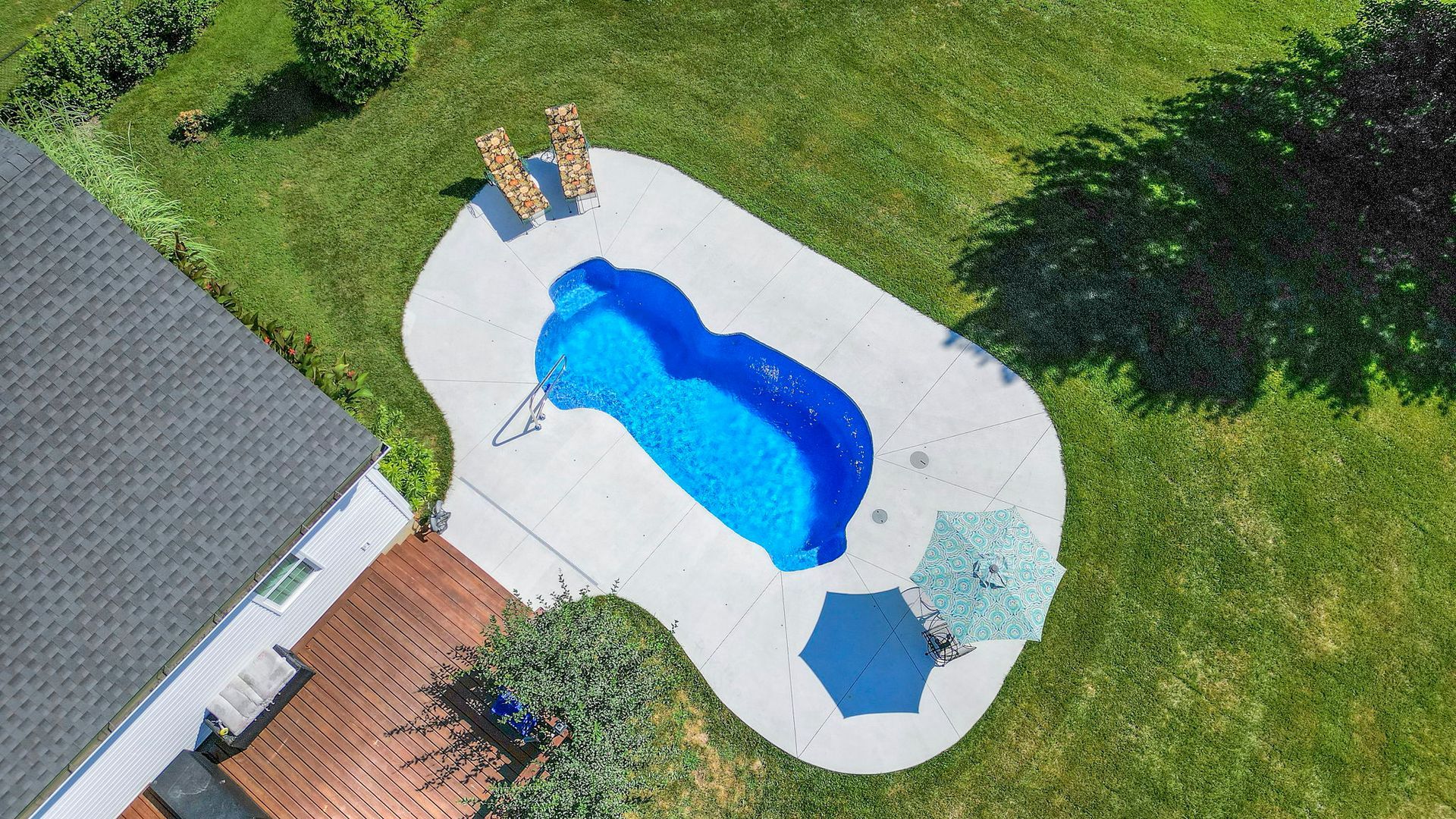 Aerial view of a swimming pool with lounge chairs and an umbrella in a backyard.
