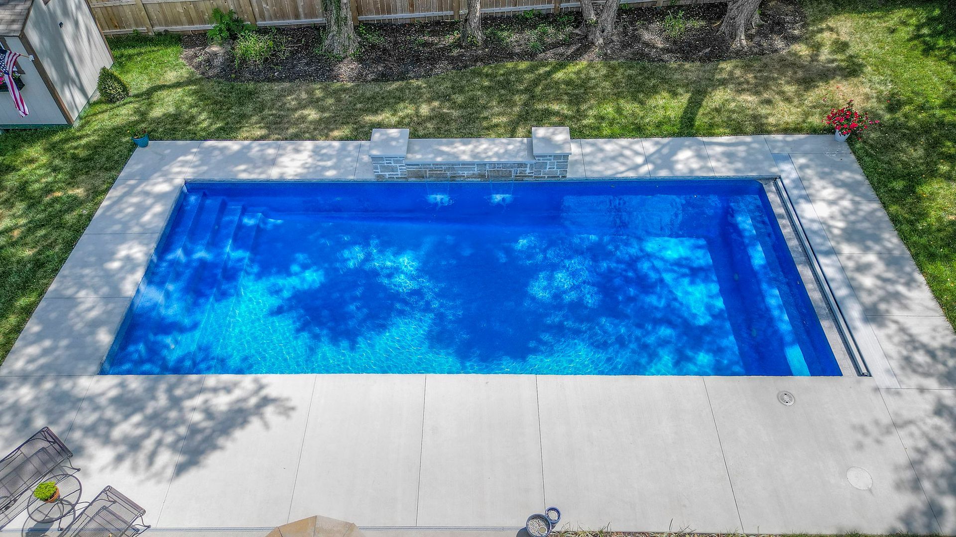 Overhead view of a rectangular pool with blue water, surrounded by gray concrete and green grass.
