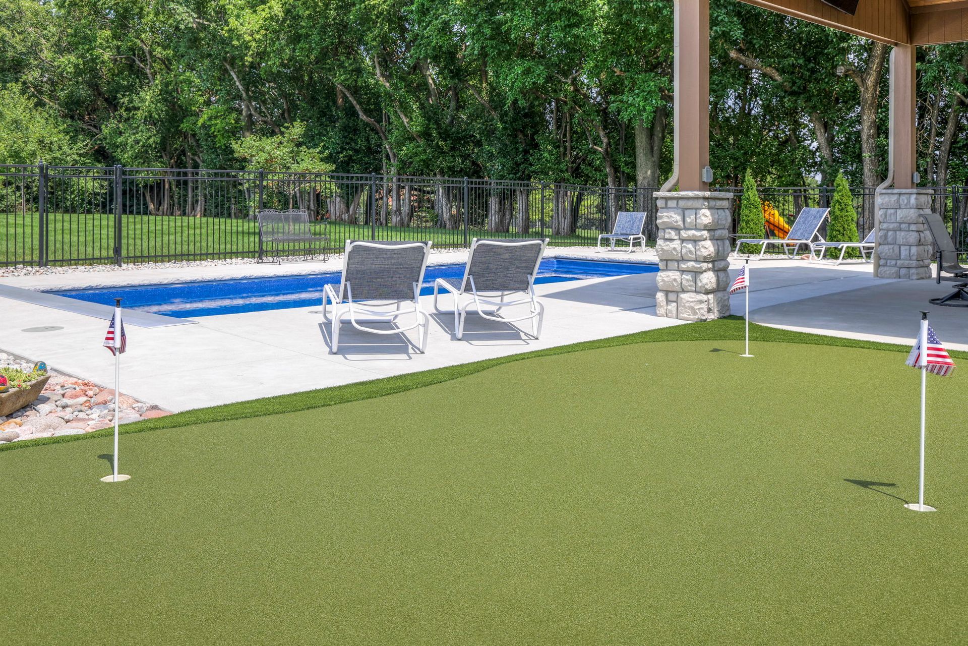 Backyard with putting green, pool, lounge chairs, and pergola.
