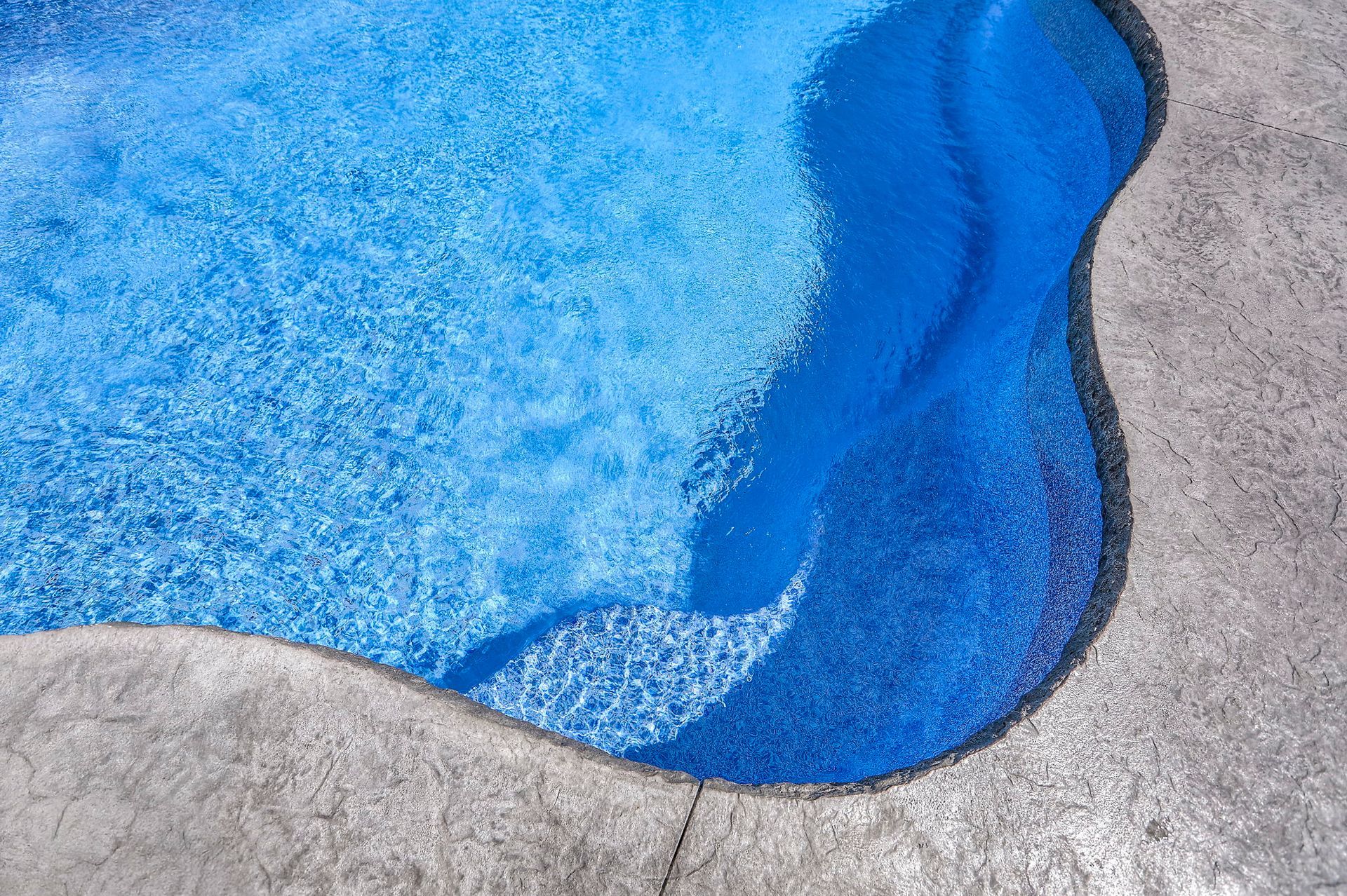 Blue pool water with steps and gray concrete edging.