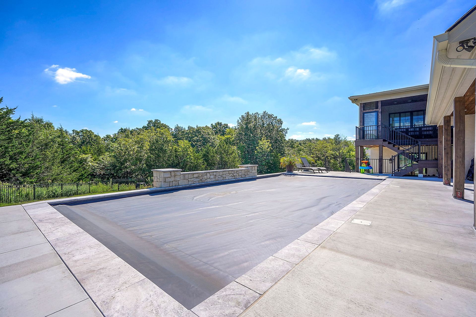 Pool covered with a gray tarp next to a house with an attached porch, under a blue sky.