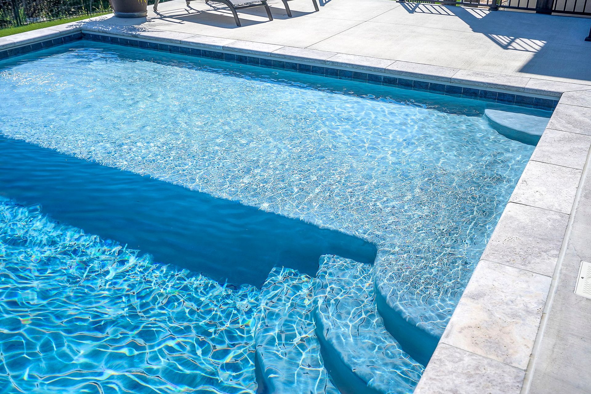 Blue rectangular swimming pool with steps, surrounded by stone patio.