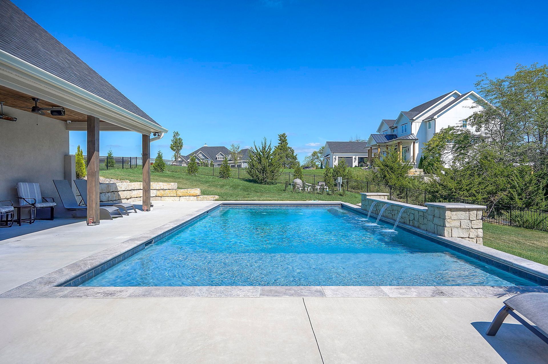 Rectangular swimming pool in backyard with stone accents. Blue water reflects bright sky.