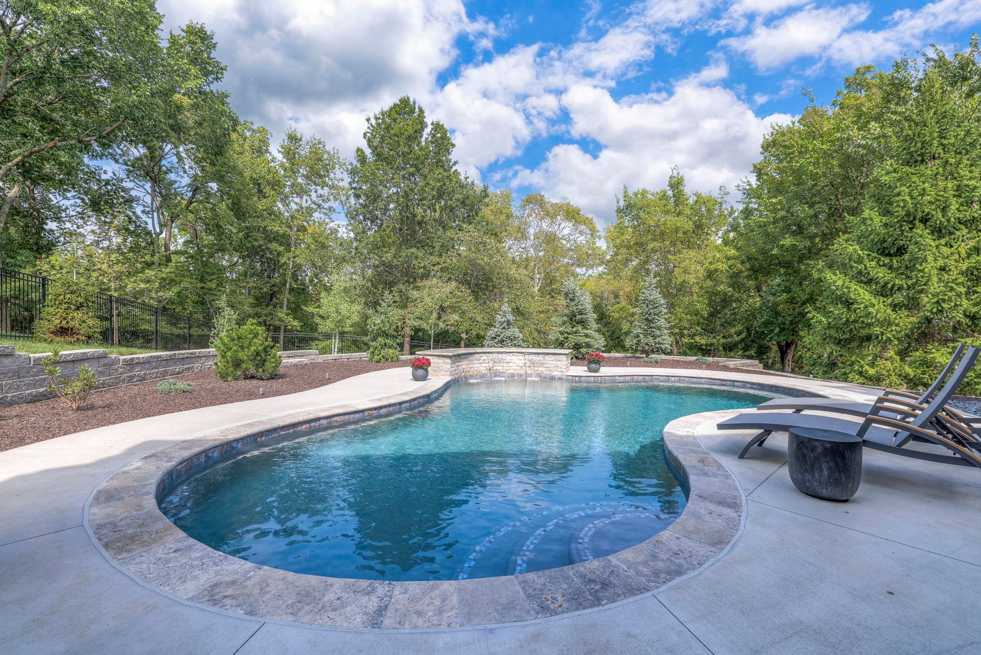 Pool with blue water and stone edge surrounded by trees and a concrete patio.