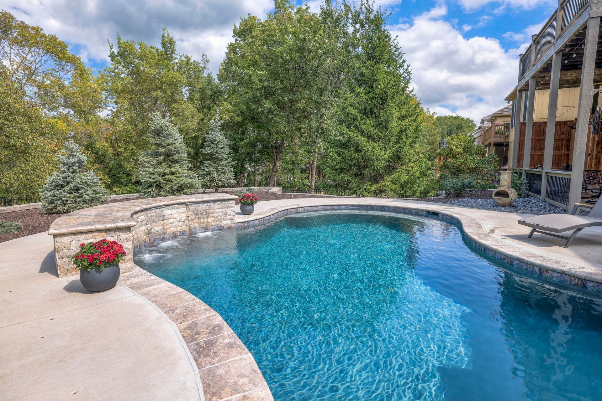 Swimming pool with turquoise water, stone coping, and lush greenery in background.