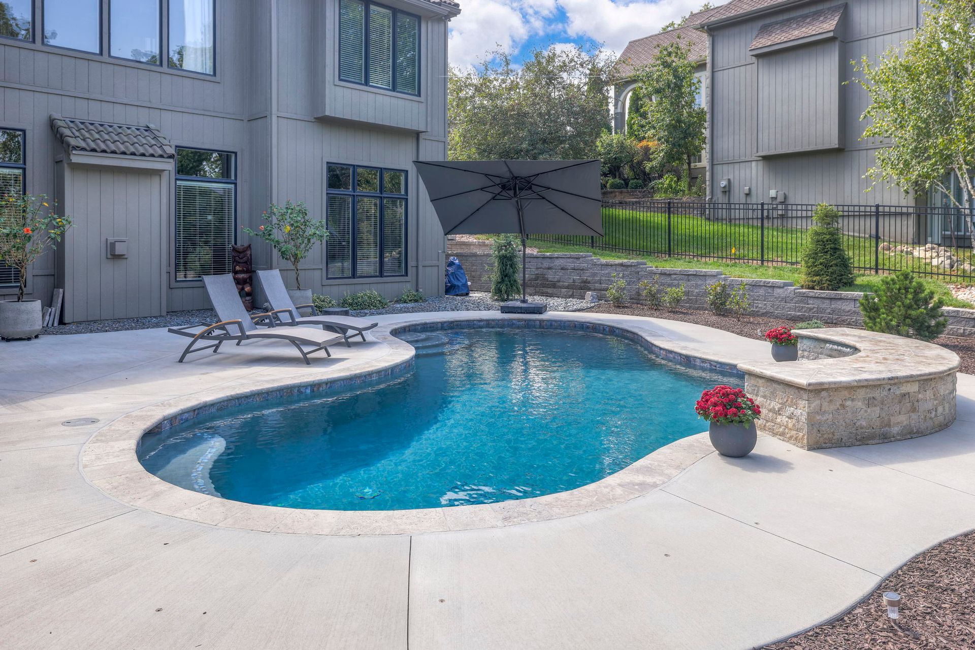 Backyard with a blue, freeform pool, patio, and home with gray siding under a cloudy sky.