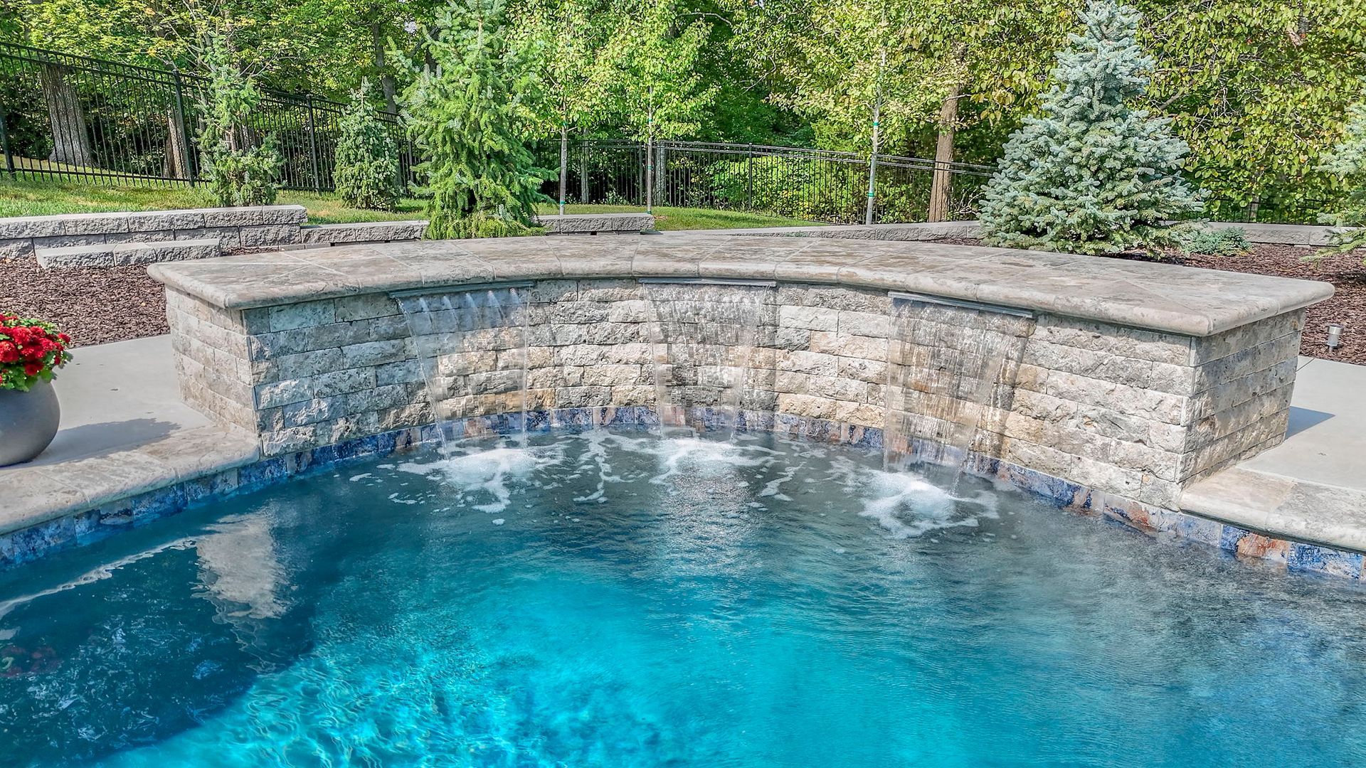 Pool with a stone waterfall feature; blue water, green trees in the background.