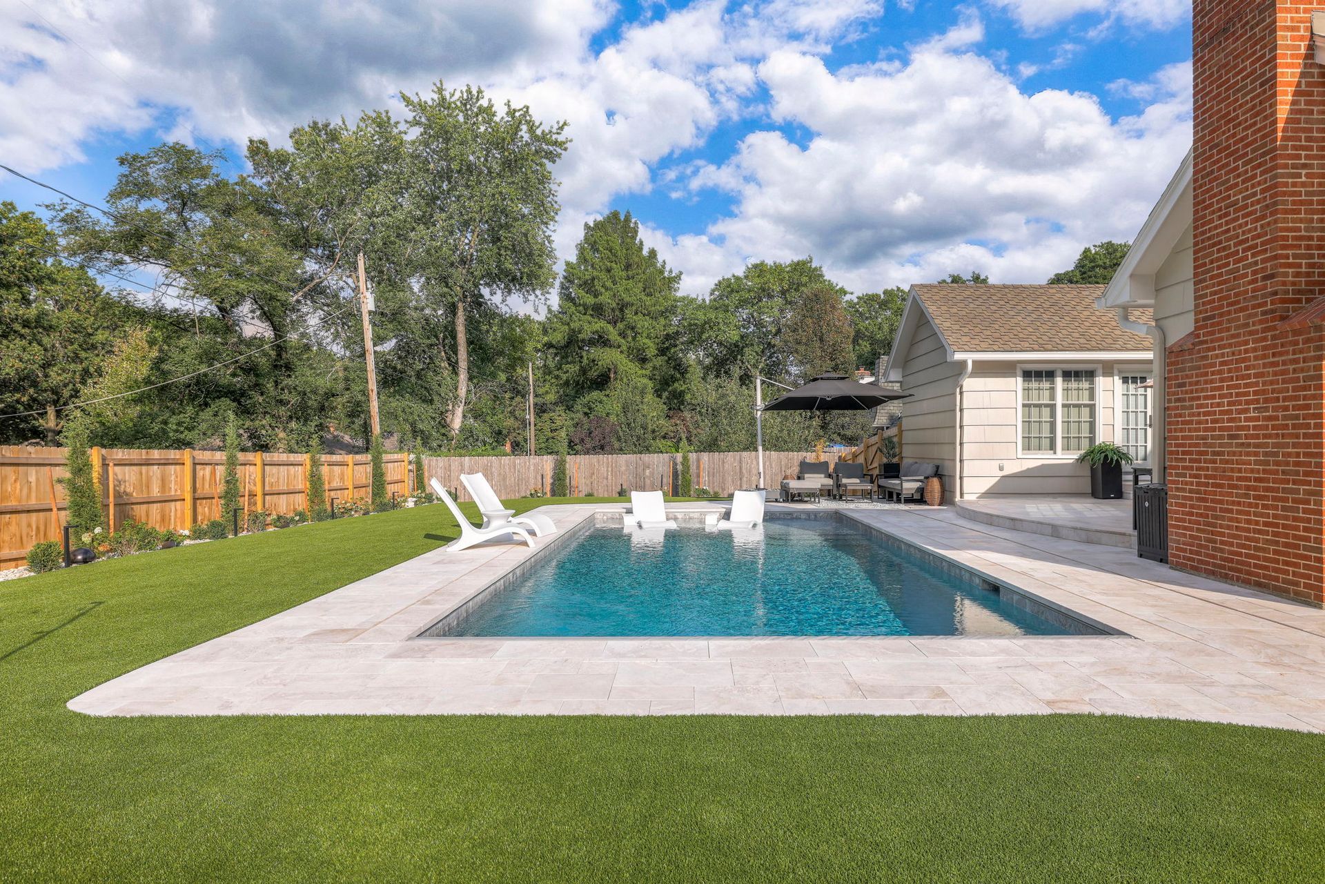 Backyard pool with white lounge chairs, green grass, and a brick chimney.