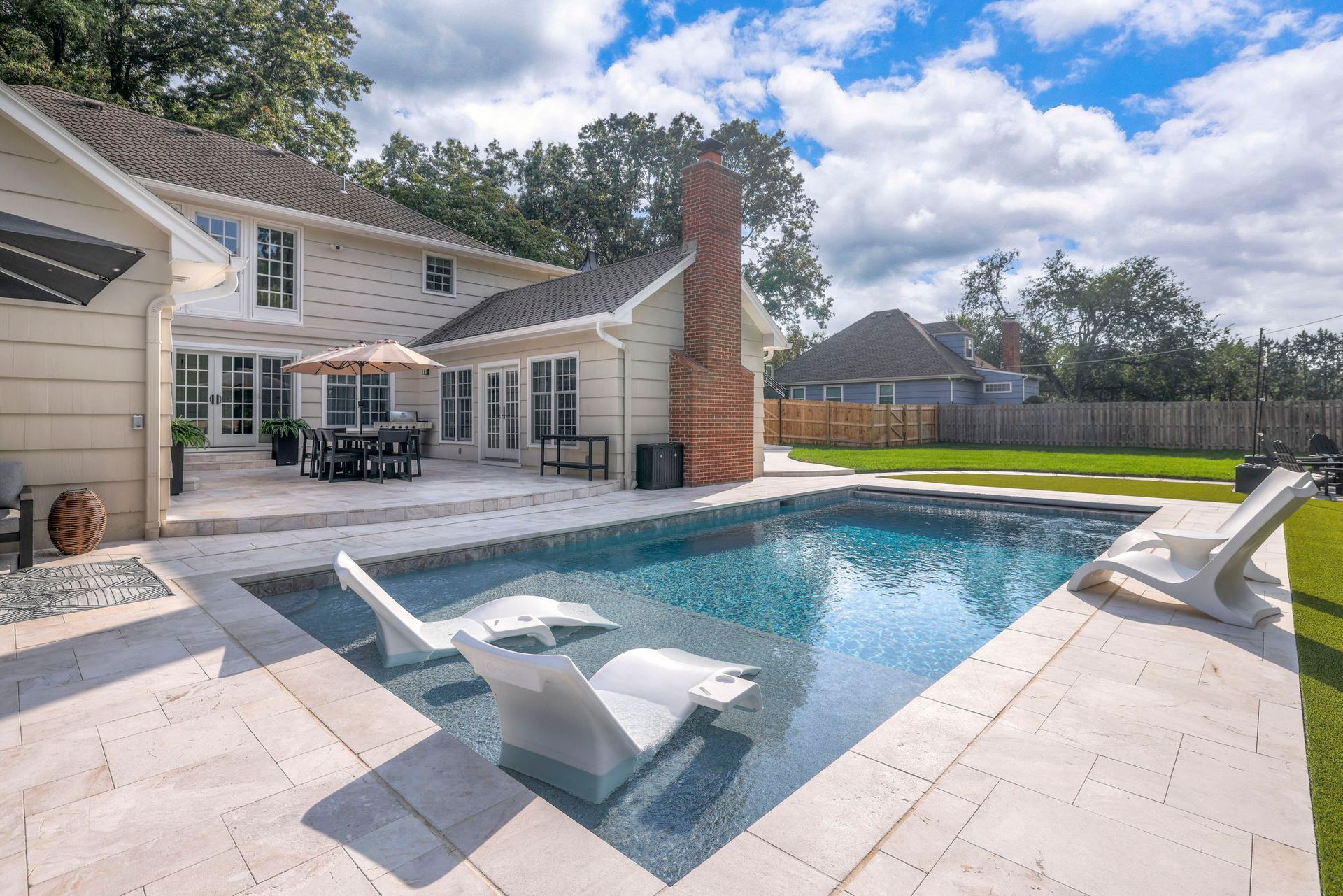 Backyard with a swimming pool, lounge chairs, and a two-story house with a patio.