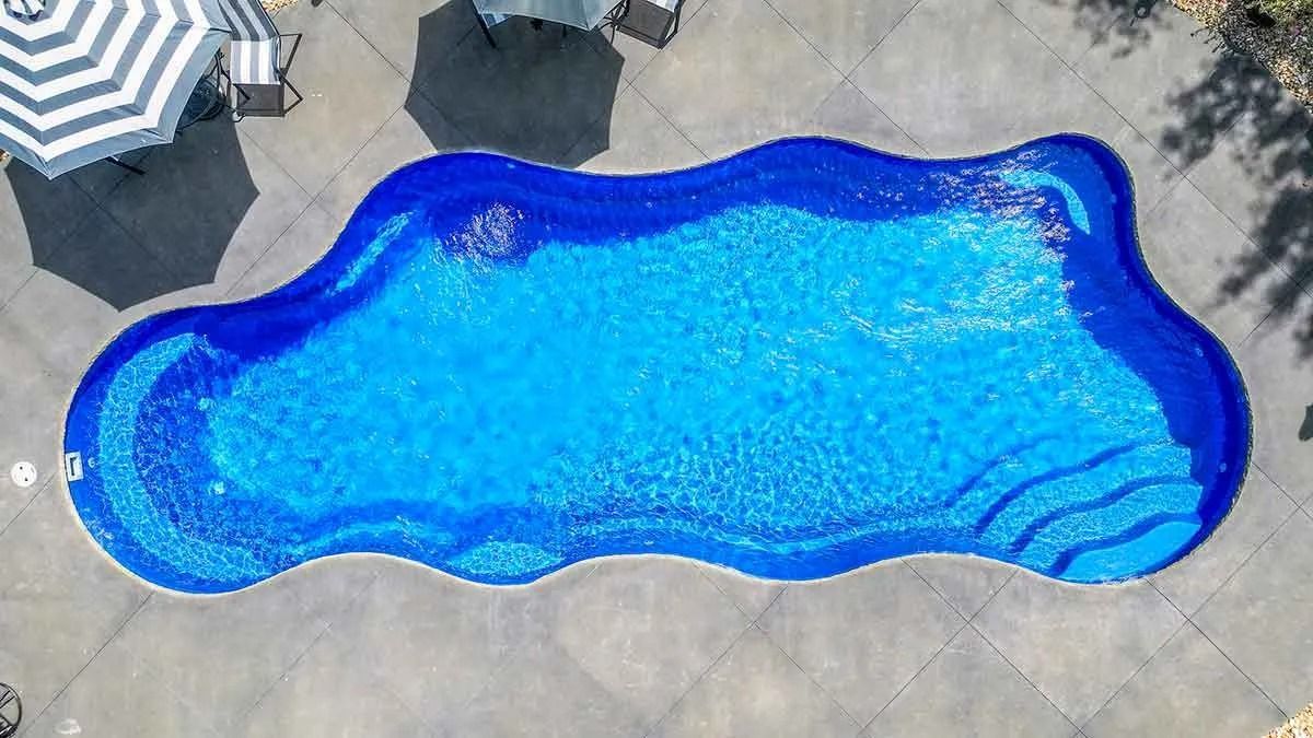 Overhead view of a kidney-shaped pool with blue water and mosaic tile trim, surrounded by concrete and a striped umbrella.