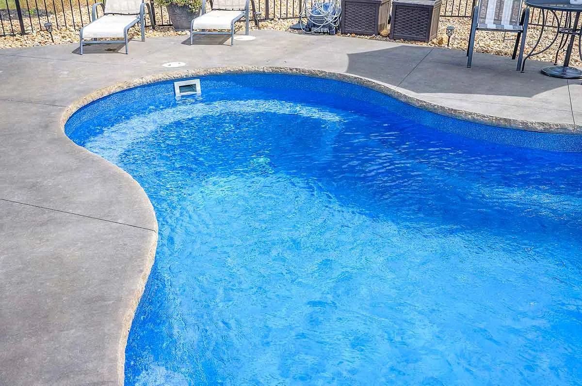 Blue swimming pool with a curved edge, surrounded by gray concrete.