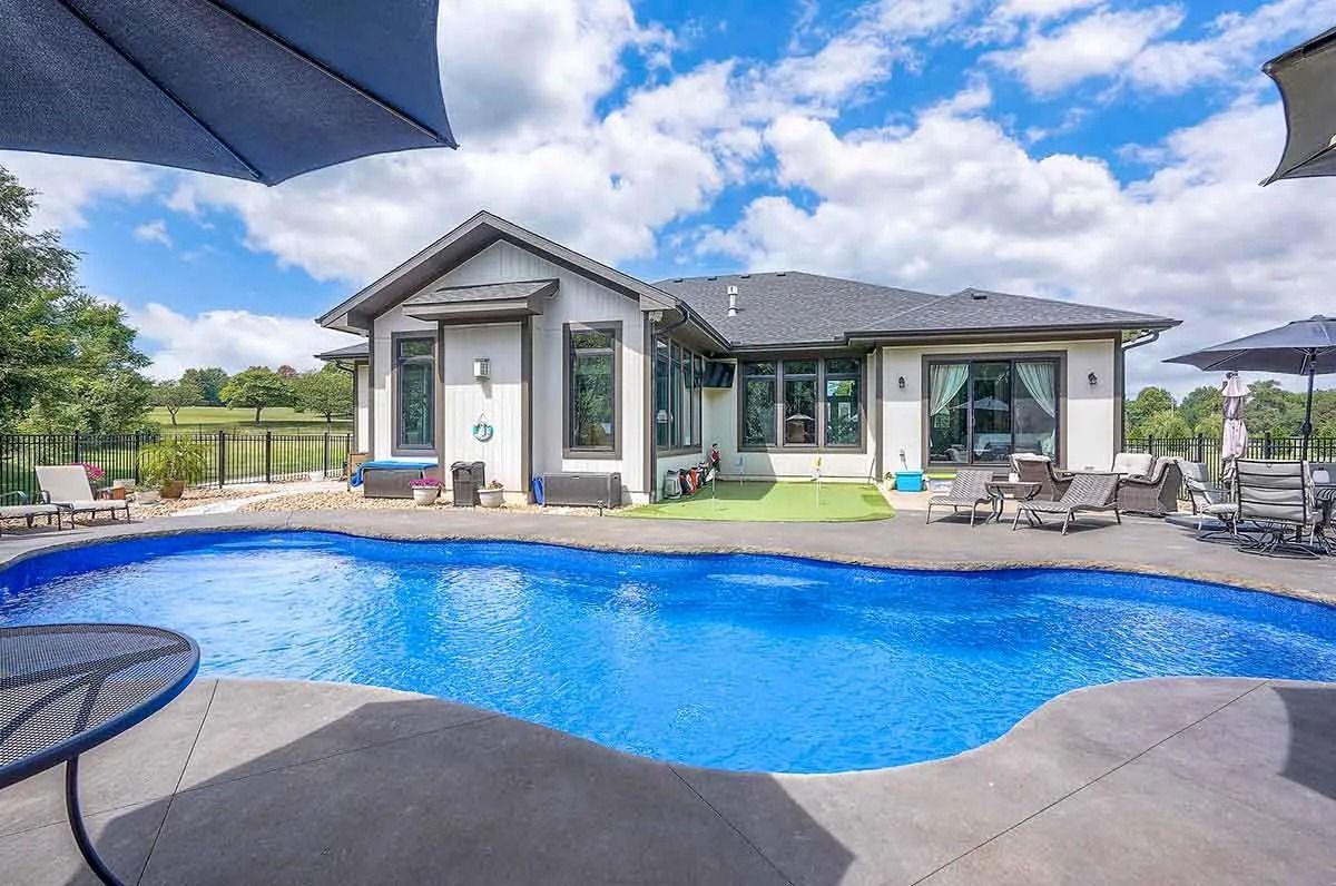 House with pool, lounge chairs, umbrellas, and blue sky.