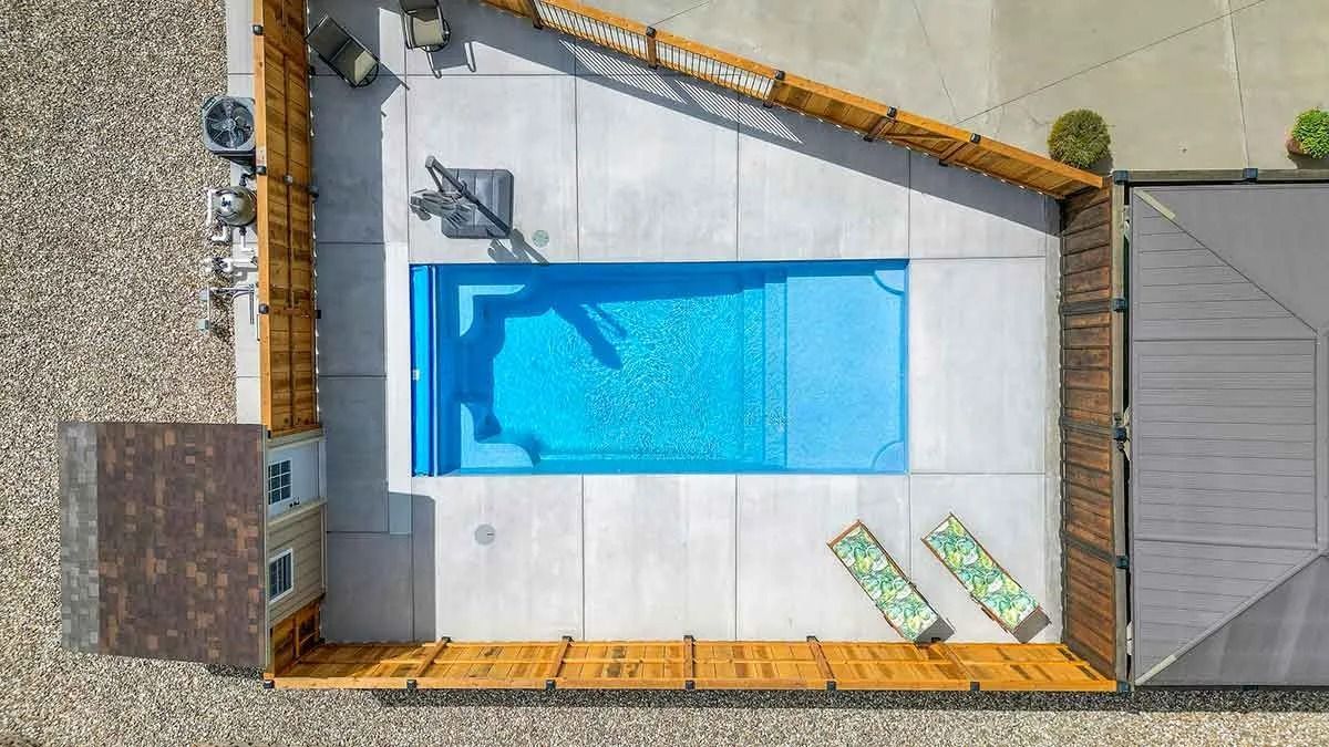 Overhead view of a rectangular pool with blue water, surrounded by a concrete patio and wooden fence.