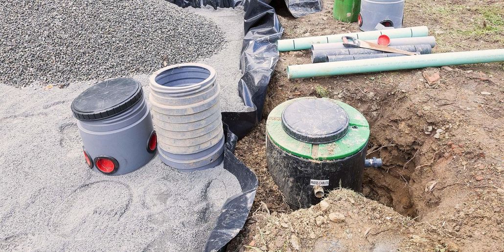 Septic system installation: Tanks, pipes, and gravel next to a hole.