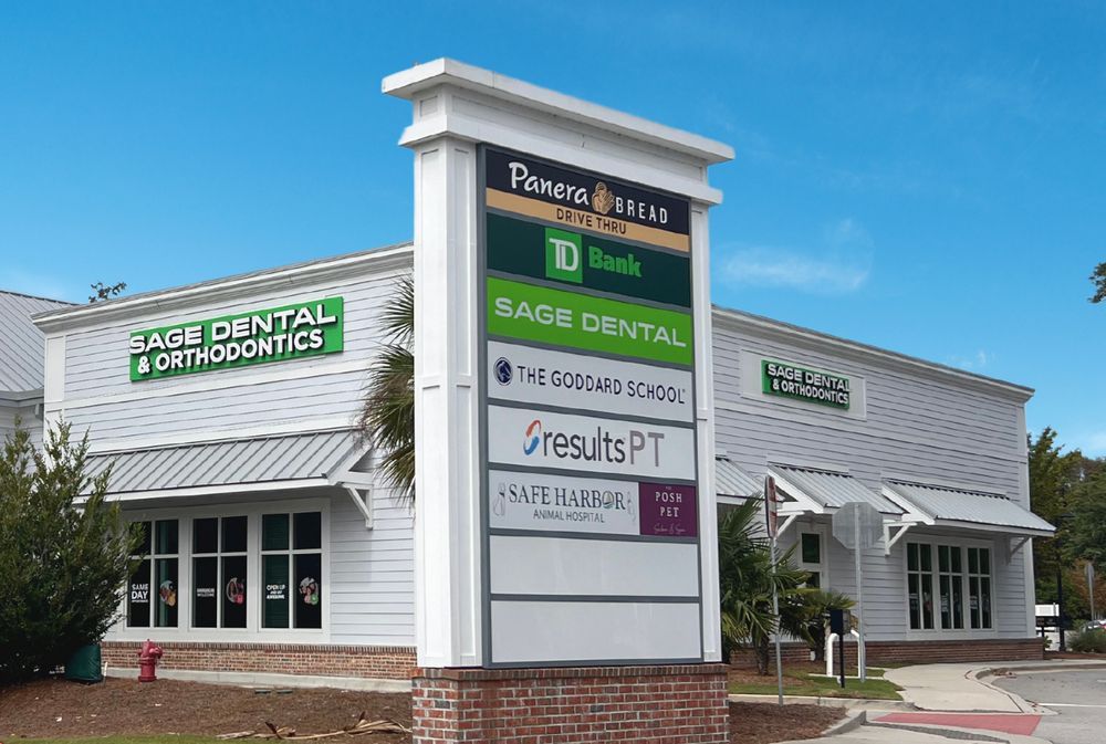 Strip mall with dental and therapy office signs under a blue sky, including Sage Dental Orthodontics and Results PT