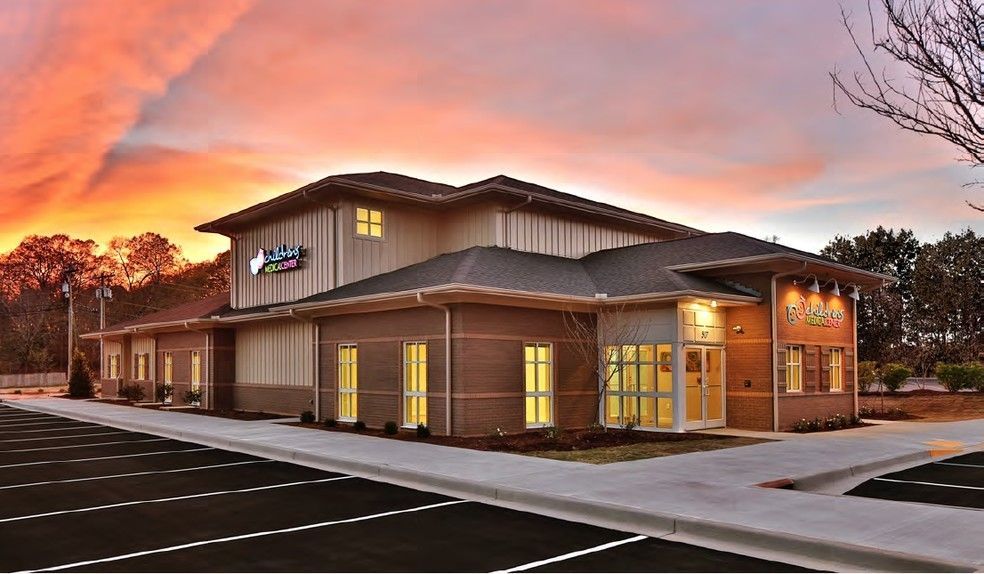Modern brick-and-stucco commercial building at dusk with lit windows and a colorful sunset sky