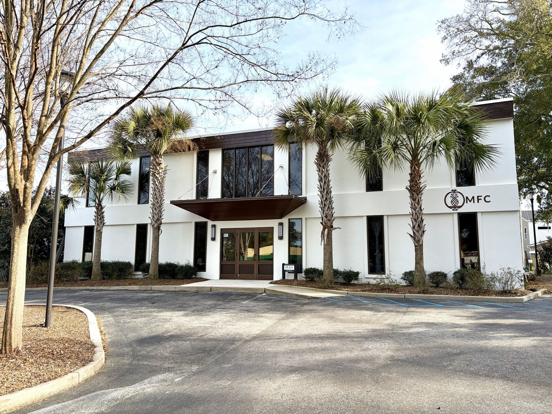 White two-story office building with dark shutters, a covered entrance, and an EMF sign, viewed from a driveway.