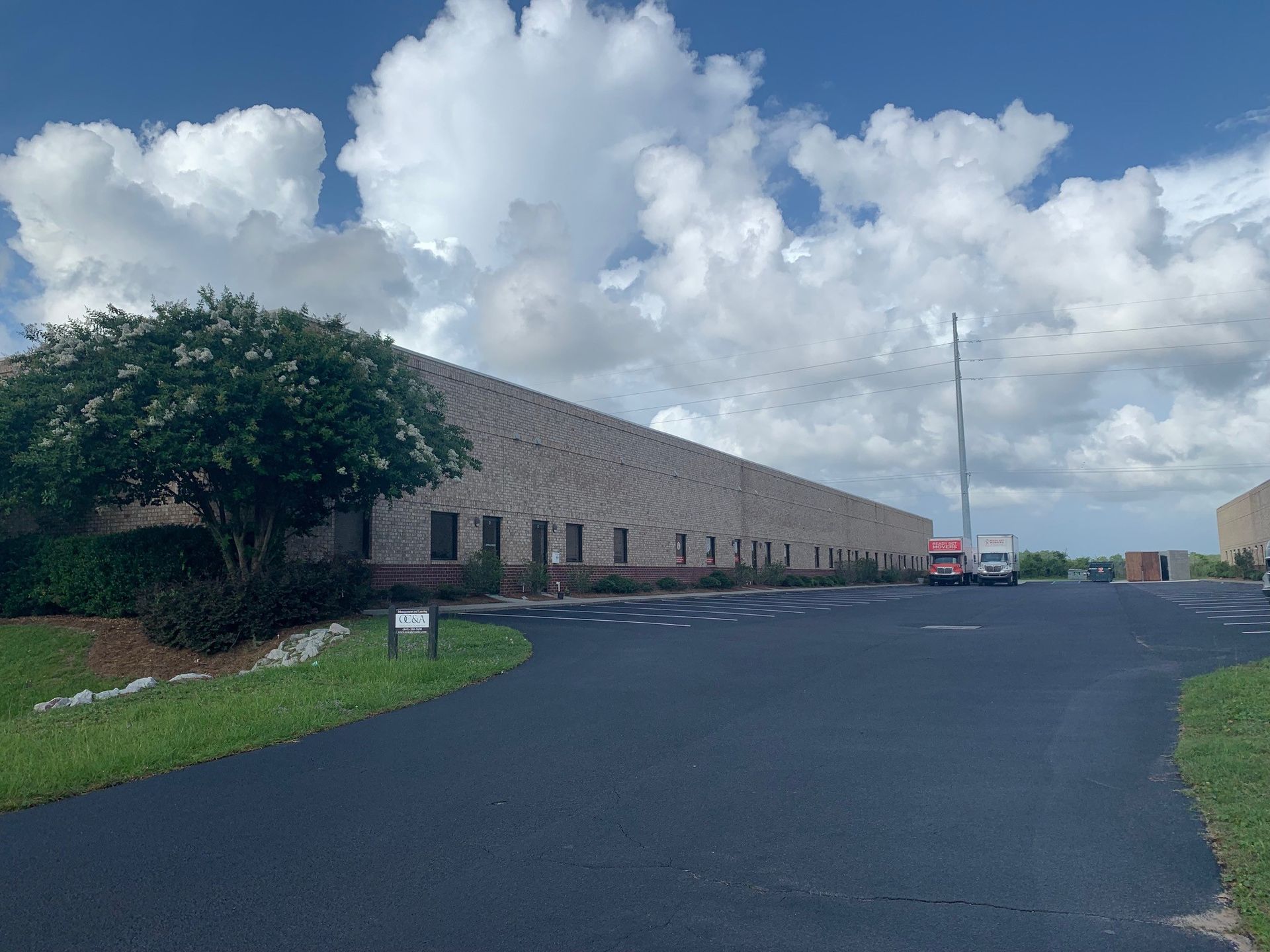 Long tan industrial building beside an empty paved lot under a cloudy sky