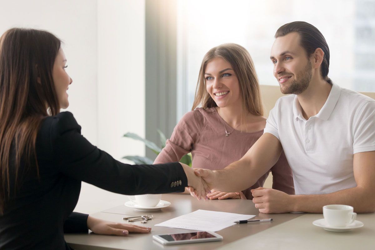 Three people shaking hands across a desk in a bright office meeting room