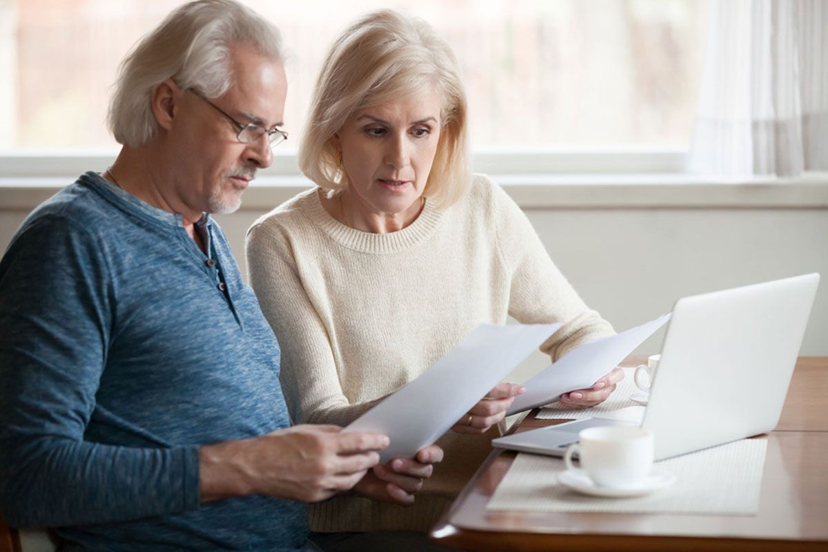 Two people reviewing papers at a table beside a laptop and coffee mug