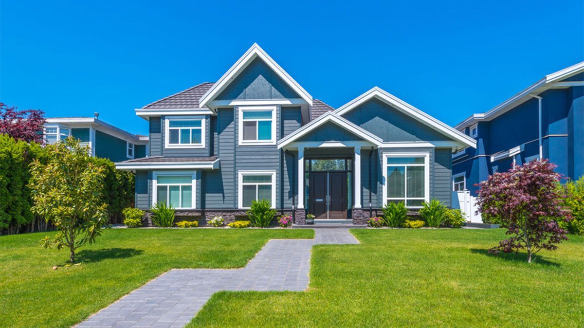 Blue suburban house with white trim, front lawn, and walkway under a clear sky
