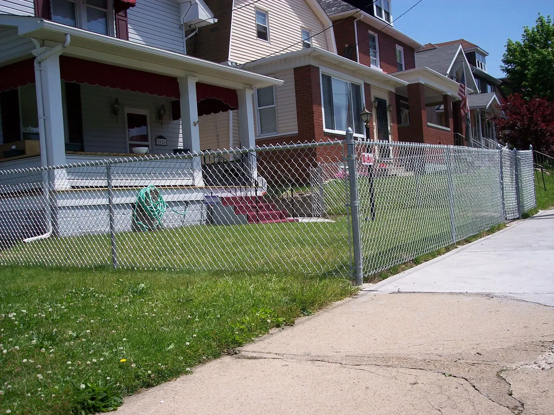 Chain link fence in front of row houses with green grass and sidewalk.