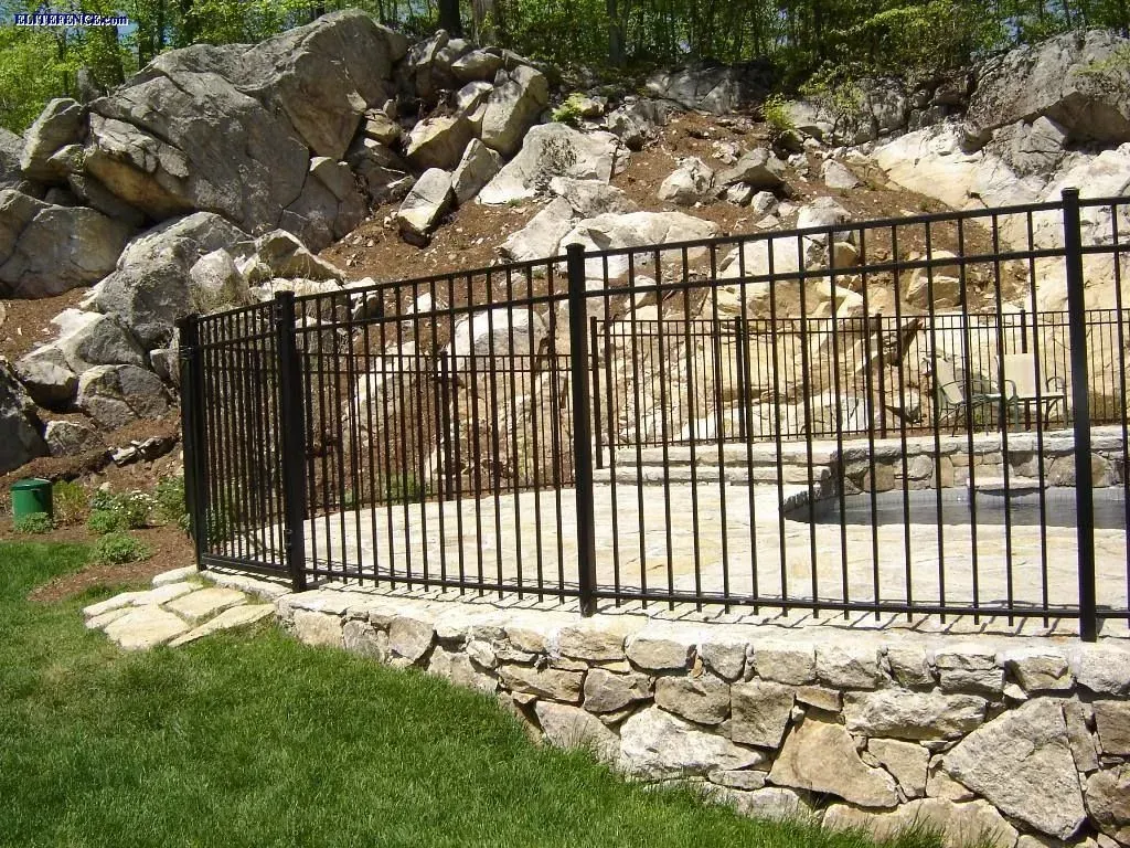 Black metal fence on stone wall; rocks in background.